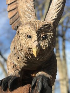 A close up shot looking at the detail of an owl wood carving on an old tree stump.