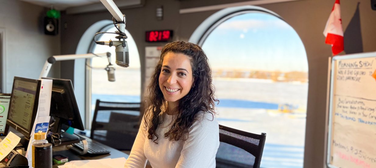 Mariam Serkal poses at her desk with the microphone in the Mix 97 studio, overlooking the Bay of Quinte