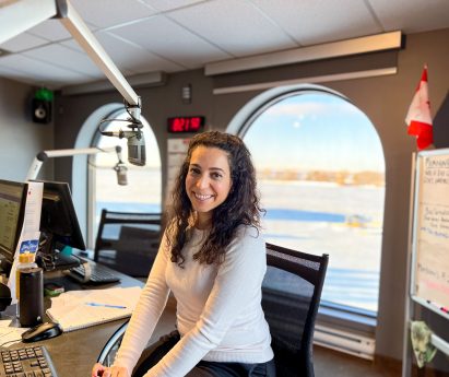 Mariam Serkal poses at her desk with the microphone in the Mix 97 studio, overlooking the Bay of Quinte