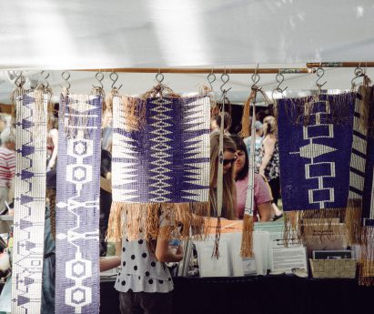A row of beaded purple and white belts hanging from a wooden rod.